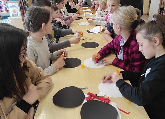 Dzieci siedzą przy stole i wykonują papierowe bociany