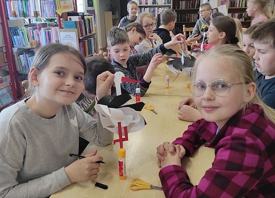 Dzieci siedzą przy stole i wykonują papierowe bociany