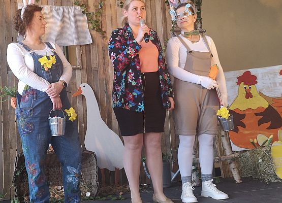 Pani wicewójt przemawia na scenie. Obok stoją dwie kobiety przebrane za króliki wielkanocne