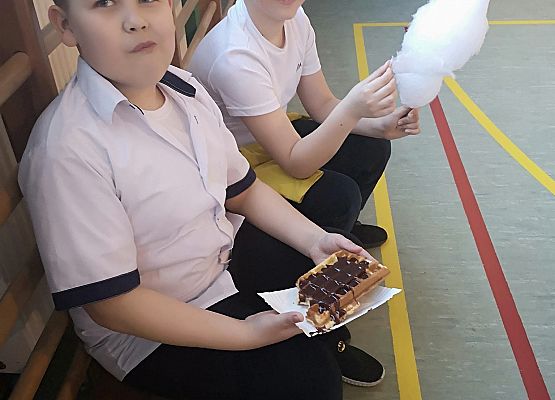 Dwaj chłopcy siedzą na łące i jedzą gofra i watę cukrową