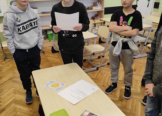 Uczennica czyta ofertę, obok stoją dwaj uczniowie