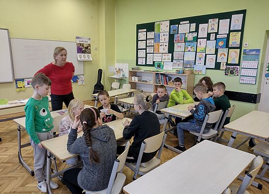 Uczniowie siedzą przy stolikach i pracują w grupach