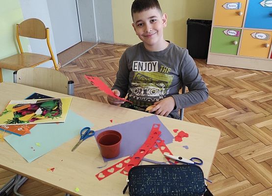 Uczniowie ozdabiają doniczki kolorowymi kwiatami z papieru