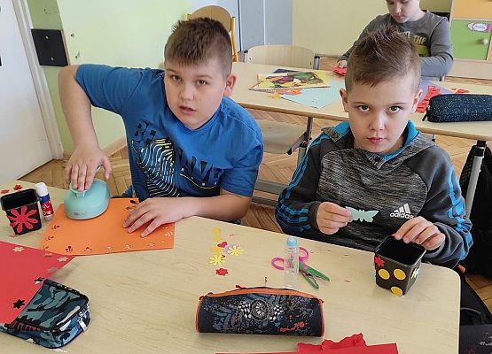 Uczniowie ozdabiają doniczki kolorowymi kwiatami z papieru