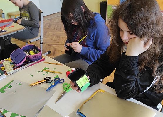 Uczniowie ozdabiają doniczki kolorowymi kwiatami z papieru