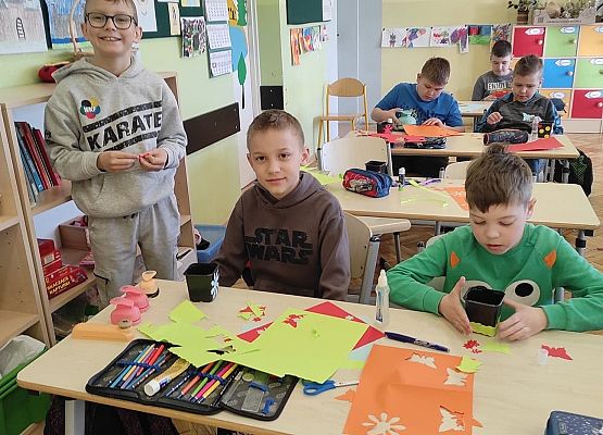 Uczniowie ozdabiają doniczki kolorowymi kwiatami z papieru