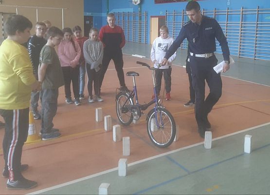 Policjant prowadzi rower obok stoją uczniowie