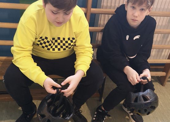 Dwaj chłopcy siedzą na ławce i trzymają kaski rowerowe