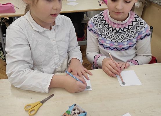 Uczennice siedzą przy stoliku i rysują ołówkami