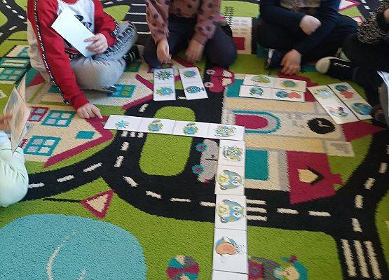 Dzieci siedzą na dywanie i grają w domino