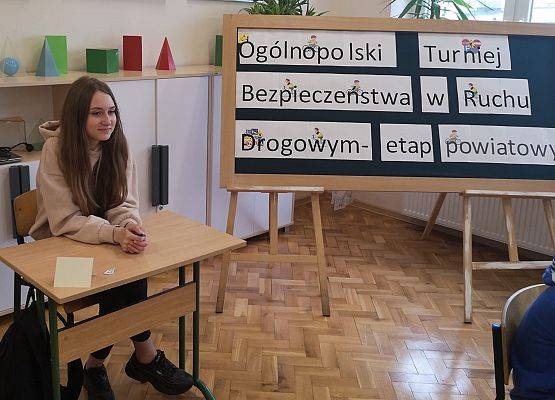 Uczennica siedzi przy stoliku, obok napis: Ogólnopolski Turniej Bezpieczeństwa w Ruchu Drogowym