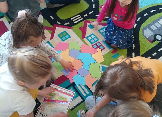 Dzieci siedzą na dywanie i układają puzzle