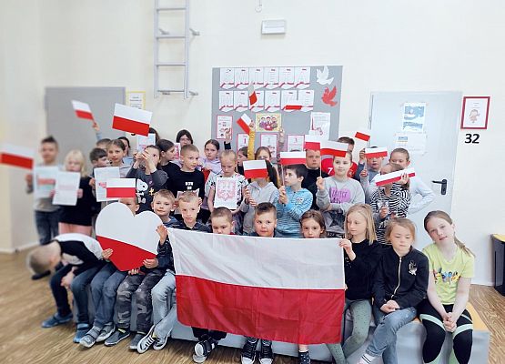 Uczniowie z flagami na tle majowej gazetki szkolnej