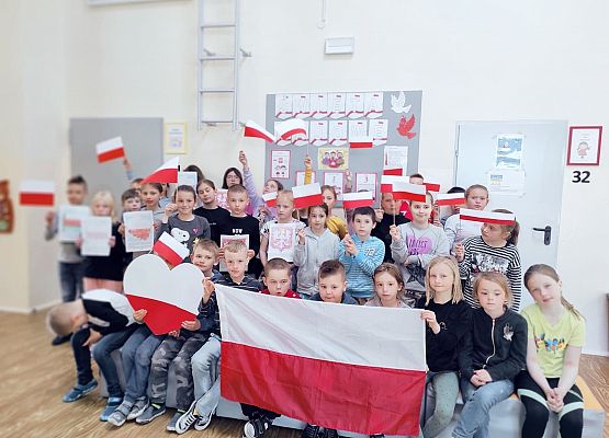 Uczniowie z flagami na tle majowej gazetki szkolnej