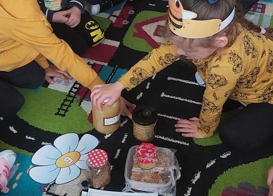 Dzieci siedzą na dywanie i oglądają miody w słoikach