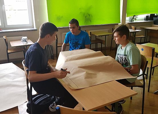 Uczniowie siedzą przy stoliku i wykonują projekt