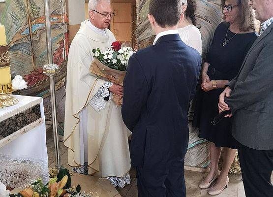 Dyrekcja z uczniami wręczają kwiaty księdzu