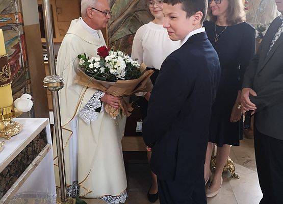 Dyrekcja z uczniami wręczają kwiaty księdzu