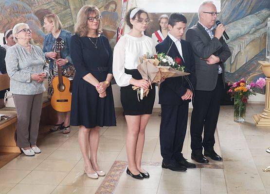 Dyrekcja z uczniami wręczają kwiaty księdzu
