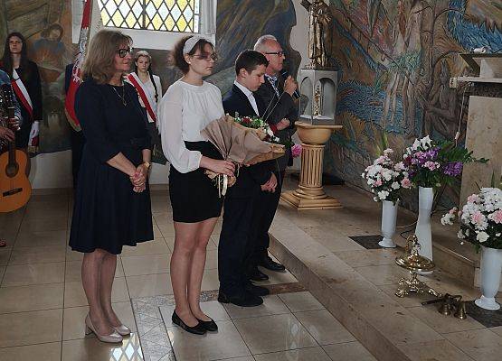 Dyrekcja z uczniami wręczają kwiaty księdzu