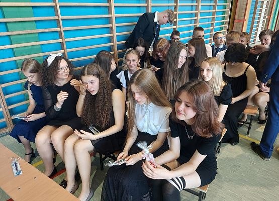 Uczniowie siedzą na ławeczkach