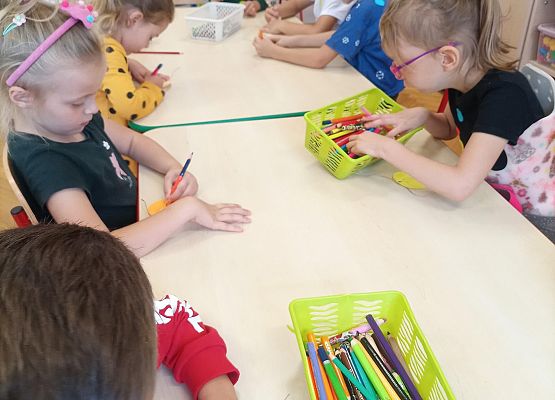 dzieci siedzą przy stoliku i wykonują prace plastyczne