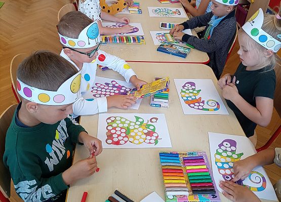 dzieci siedzą przy stoliku i wykonują prace plastyczne