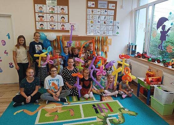 Grupa dzieci z przedszkola i uczennice z Samorządu Uczniowskiego prezentują zakręcone balony
