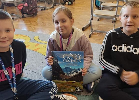 Dzieci siedzą na podłodze i prezentują książkę o górach