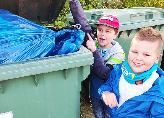 Chłopcy wyrzucają do kontenera worek ze śmieciami