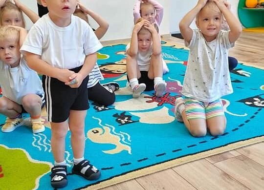 Przedszkolaki w strojach gimnastycznych ćwiczą