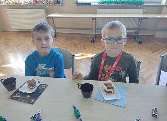 Dwaj chłopcy siedzą przy stoliku podczas słodkiego poczęstunku