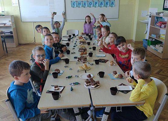 Uczniowie siedzą przy wspólnym stole podczas słodkiego poczęstunku