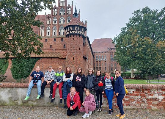Uczniowie z wychowawcą stoją przed Zamkiem w Malborku