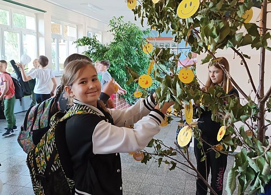 Uczennica zawiesza emotikonę uśmiechu na drzewie szczęścia
