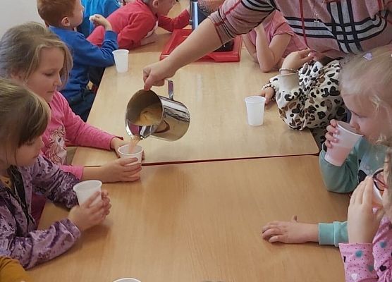 Nauczycielka rozlewa w kubeczki sok dla dzieci