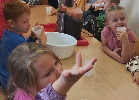 Dzieci siedzą przy stoliku i piją sok