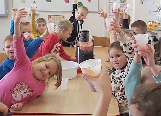 Dzieci siedzą przy stoliku i piją sok