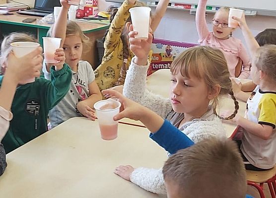 Dzieci siedzą przy stoliku i piją sok