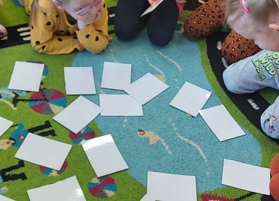 Dzieci siedzą na dywanie i bawią się kartami