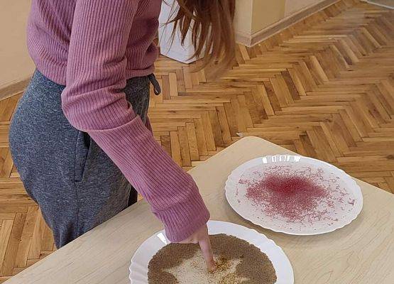 Uczennica wykonuje eksperyment z wodą, mydłem i pieprzem