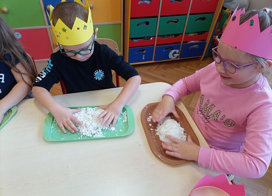 Dzieci w koronach na głowie bawią się masą plastyczną