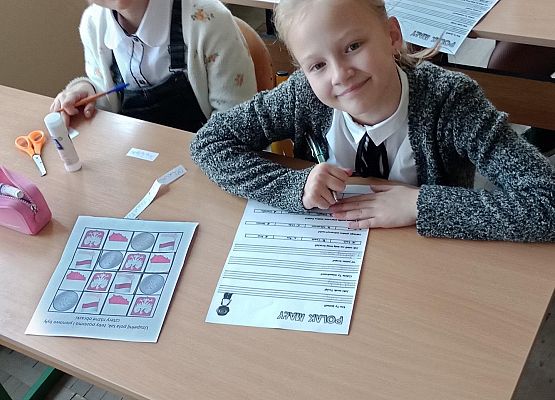 Uczennice siedzą przy stolikach i wykonują zadania