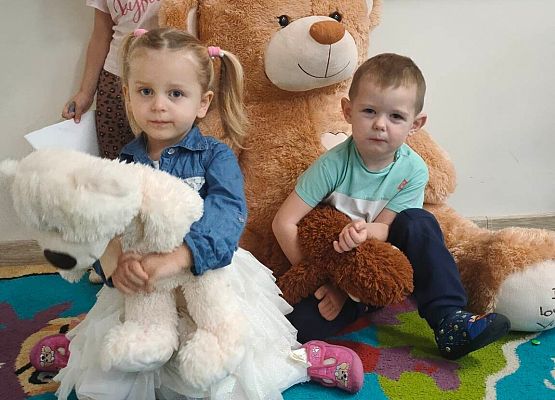 Dzieci siedzą przy pluszowym misiu
