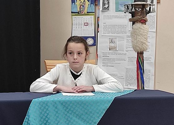 Uczestniczka konkursu siedzi przy stole i czyta tekst