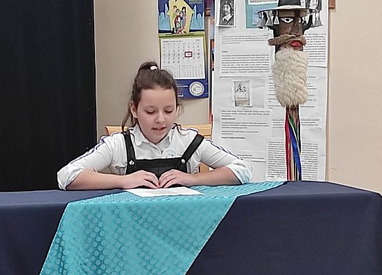 Uczestniczka konkursu siedzi przy stole i czyta tekst