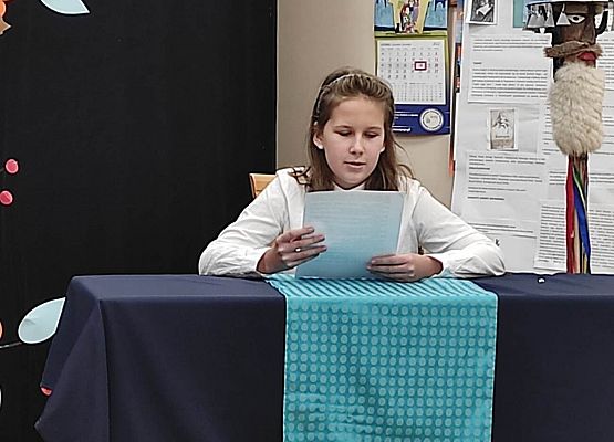 Uczestniczka konkursu siedzi przy stole i czyta tekst