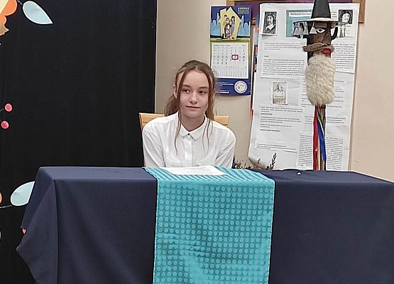 Uczestniczka konkursu siedzi przy stole i czyta tekst