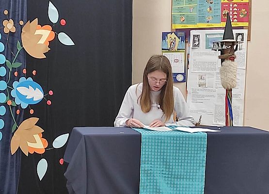 Uczestniczka konkursu siedzi przy stole i czyta tekst