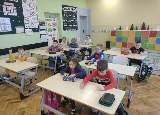 uczniowie siedzą w ławkach i prezentują różne mimiki twarzy